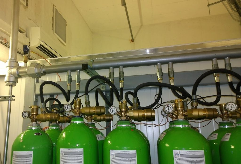 Agnitar Inert Fire Suppression system A row of bright green industrial gas cylinders connected by black hoses and brass valves, mounted against a light-colored wall in an industrial room.